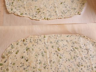 Rolled out seeded cracker dough on parchment paper.